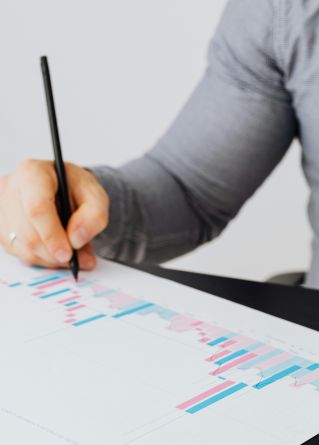 Person writing on a graph paper with colorful data bars and charts.